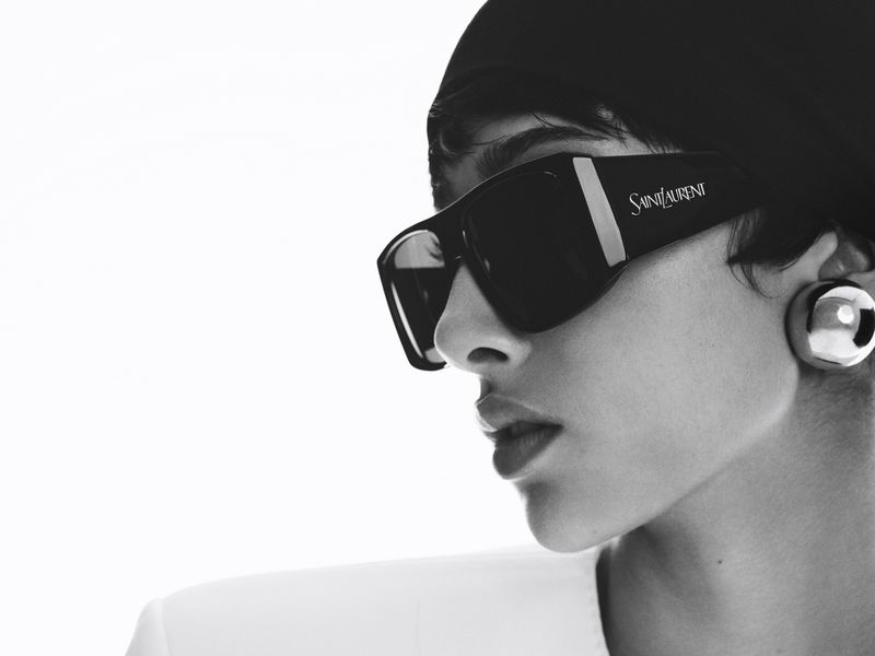 Close-up studio shot of a woman wearing sunglasses and a headscarf, looking to the side, in black and white with a minimalist aesthetic.