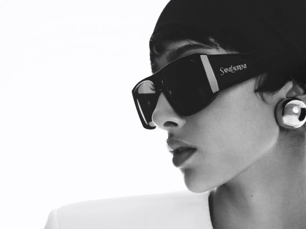 Close-up studio shot of a woman wearing sunglasses and a headscarf, looking to the side, in black and white with a minimalist aesthetic.