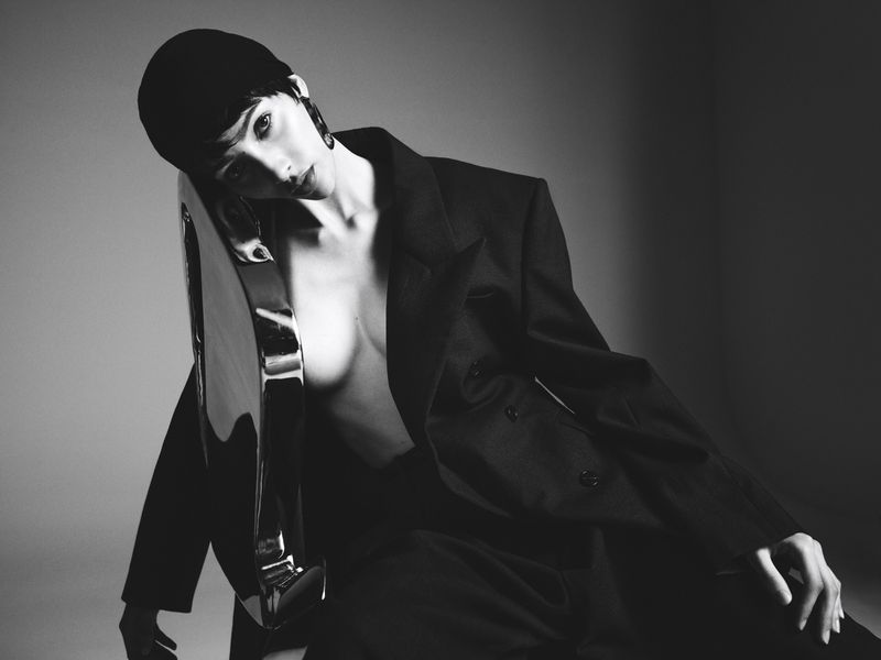 Monochrome portrait of model Yasmin Wijnaldum wearing a dark blazer leaning against a metallic object in a studio