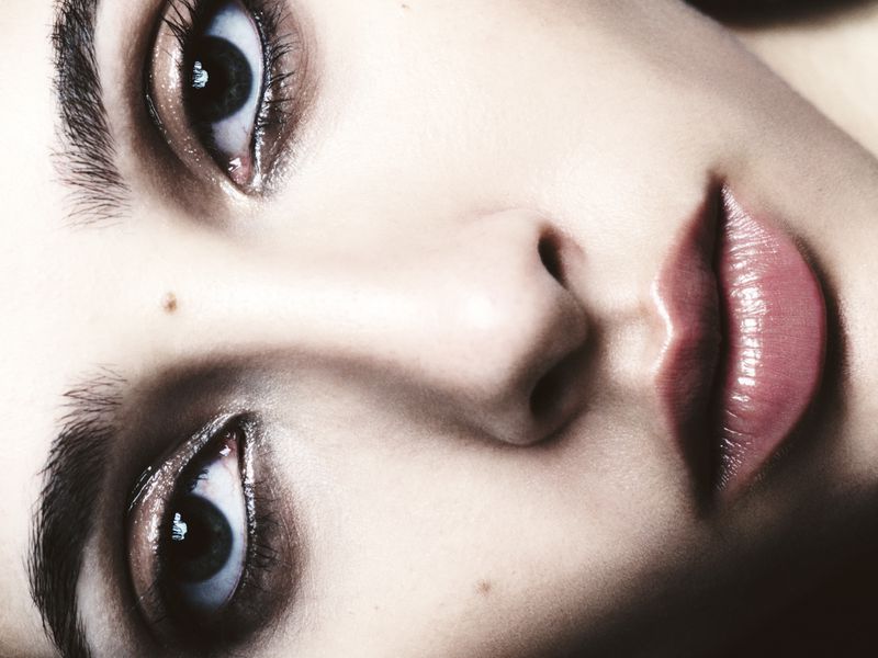 Close-up portrait of a person's face with blue eyes, full glossy lips, and fair skin, with selective focus and soft lighting.