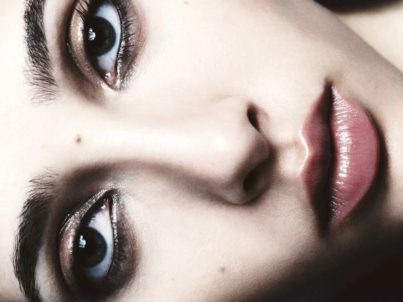 Close-up portrait of a person's face with blue eyes, full glossy lips, and fair skin, with selective focus and soft lighting.
