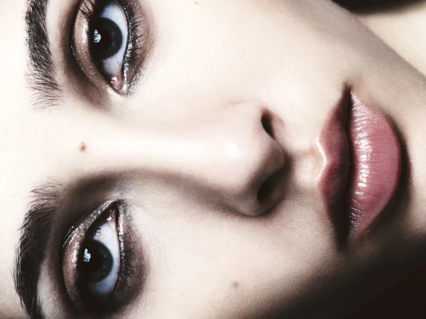 Close-up portrait of a person's face with blue eyes, full glossy lips, and fair skin, with selective focus and soft lighting.