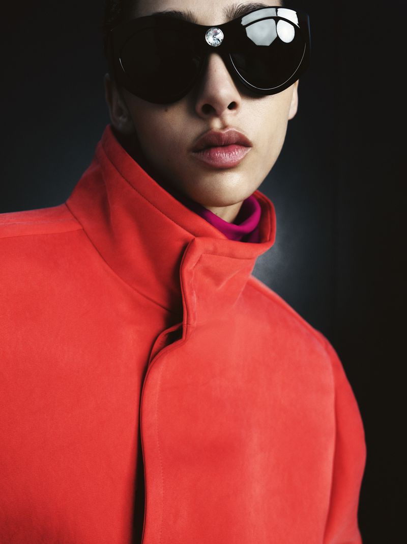Fashion portrait of a person with sunglasses and an orange coat against a dark background, showcasing beauty and style.