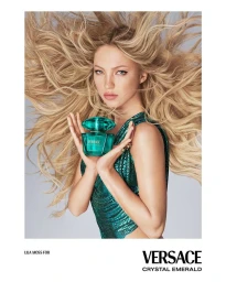 Model Lila Moss holding Versace Crystal Emerald fragrance bottle with blonde hair flowing against grey background