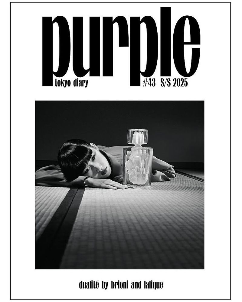 Magazine cover featuring an adult female model laying next to a perfume bottle on a patterned mat in a photo studio in black and white.