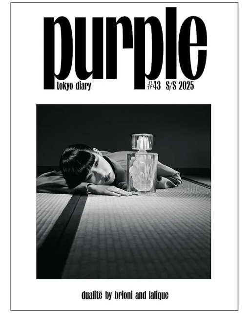 Magazine cover featuring an adult female model laying next to a perfume bottle on a patterned mat in a photo studio in black and white.