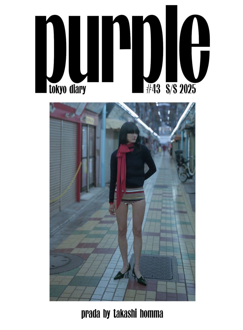 Magazine cover featuring a woman in a black top, striped bottoms, and red scarf standing in an urban alleyway for Purple magazine.
