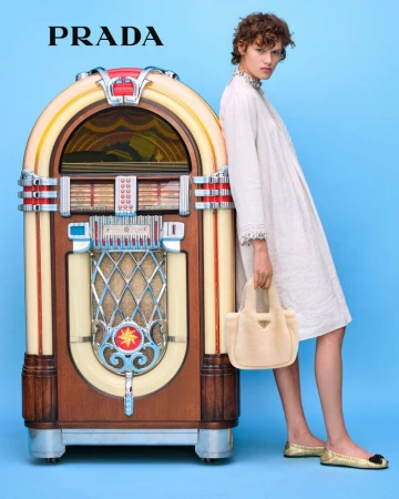 Fashion shot featuring a model in a white dress with a beige handbag next to a vintage jukebox against a light blue background.
