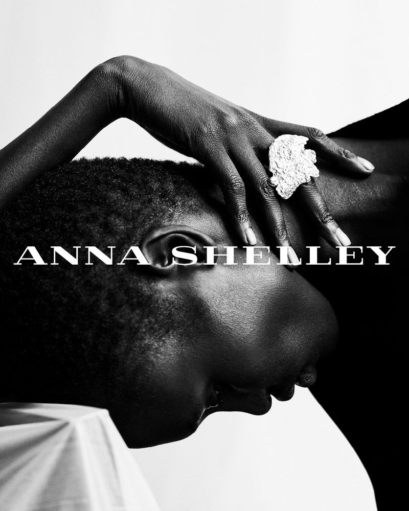Monochrome portrait of a Black woman with a large decorative ring resting her hand on her head in a photo studio setting.