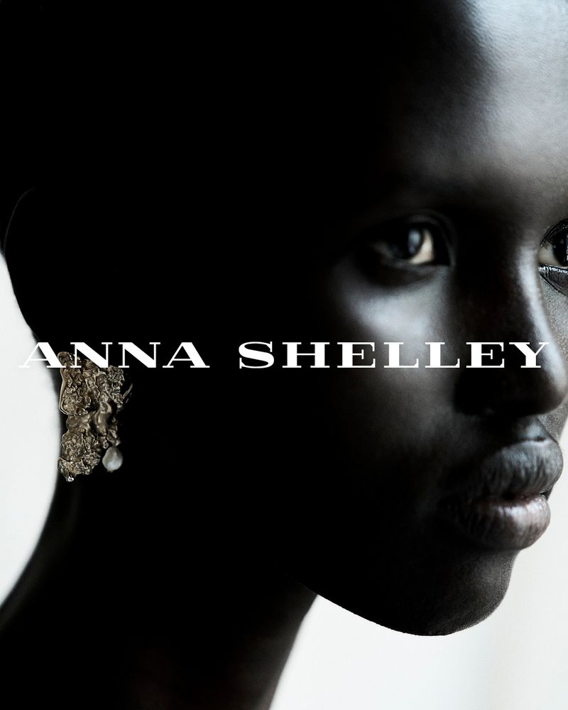 Close-up portrait of an African-American woman with dark skin, wearing a dangling earring, against a shadowed black and white background.