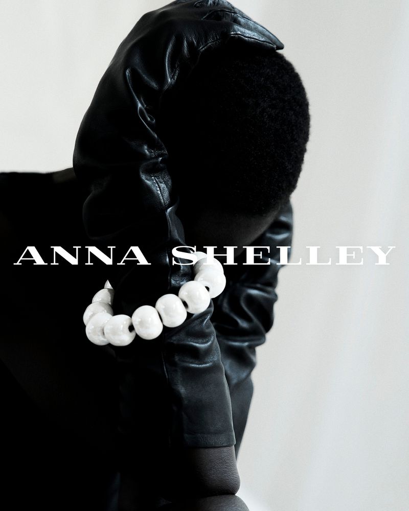 Elegant studio shot of an adult wearing black leather gloves and a white beaded bracelet against a clean white backdrop.