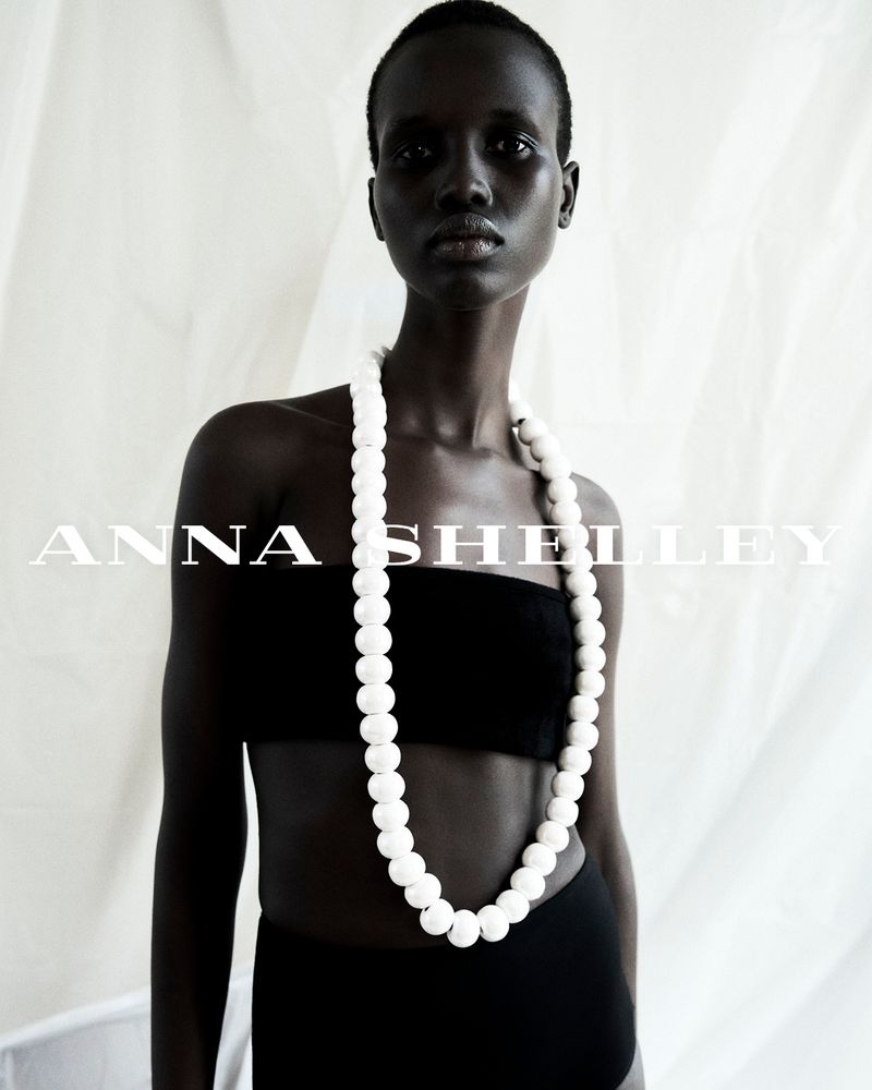 Fashion shot of an African-American adult female model wearing a black bandeau top and skirt, accessorized with a white beaded necklace.