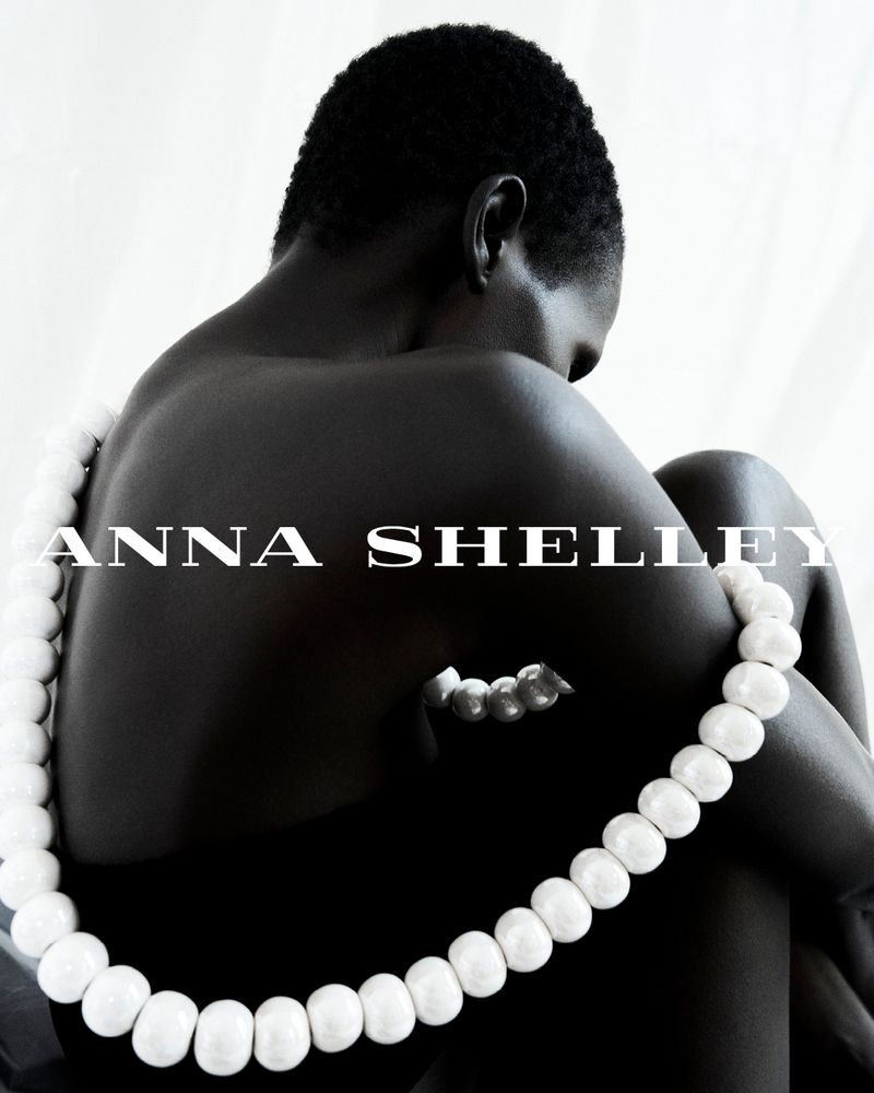 Striking studio portrait of an African American woman adorned with a white beaded necklace against a clean, white backdrop.