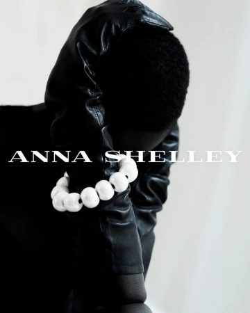 Amar Akway wearing a chunky white beaded bracelet and black leather hood against a white background for Anna Shelley.