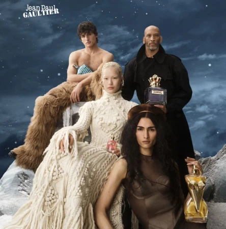 Group of four fashion models with perfume bottles in an outdoor studio setting with faux fur and cloudy sky backdrop. Jean Paul Gaultier ad.
