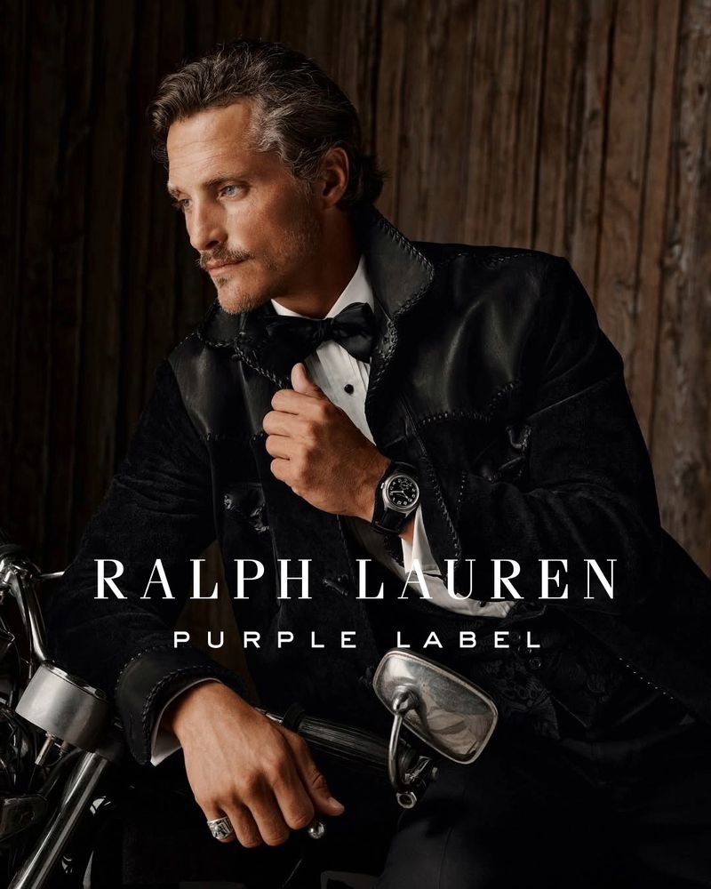 Mature man in a black tuxedo and bowtie sitting on a motorcycle, looking left with a wooden background. Ralph Lauren Purple Label ad.