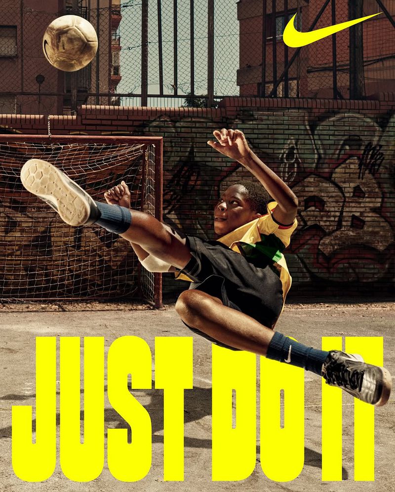 A youth soccer player in action, kicking a soccer ball with dynamic motion in an urban setting for a Nike ad. "Just Do It" text is prominent.
