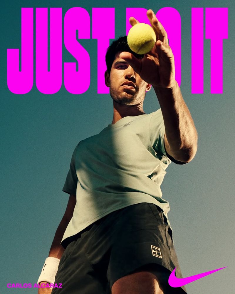 Male tennis player, Carlos Alcaraz, holding a tennis ball in an upward shot with the Nike logo and 'Just Do It' tagline.