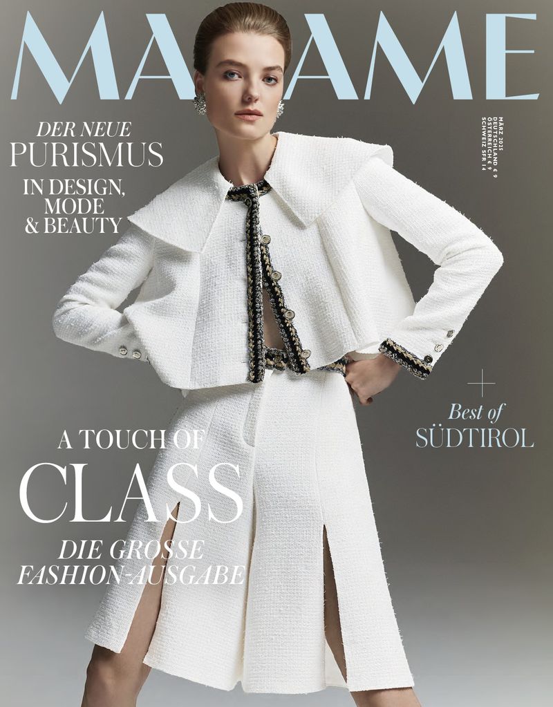 Fashion magazine cover featuring a model in a textured white suit with a jacket and skirt with thigh slits against a gray backdrop.