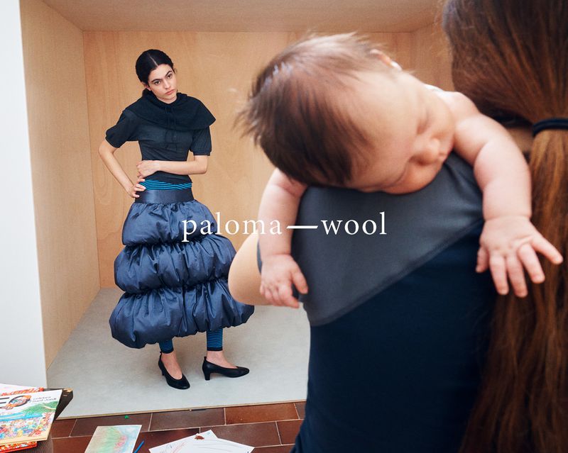 Fashion shot of a woman in a tiered skirt and baby being held by an adult in an indoor photo studio setting.