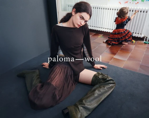 A woman in olive thigh-high boots and a brown dress is seated near a girl in a red and black flamenco dress indoors.