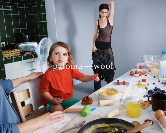Indoor scene features a child in an orange shirt at a kitchen table with a model in black mesh standing in the background.