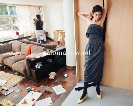 A woman in a gray dress poses next to a wooden wall, juxtaposed with a messy living room scene featuring a woman holding a baby.