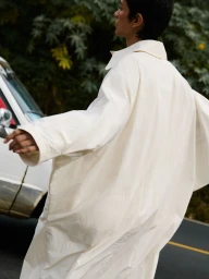 Model Marsella Rea wearing an oversized cream coat, photographed in profile beside a white vehicle for Cordera Resort 26.
