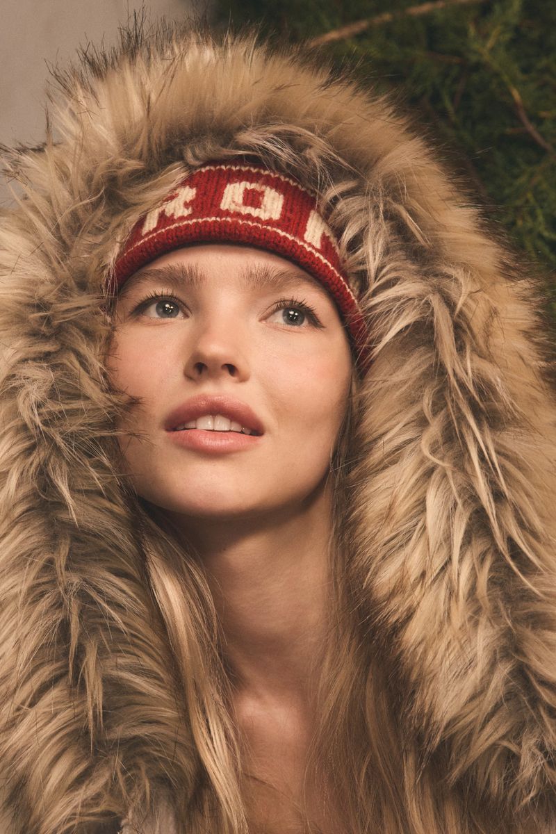 Close-up of a woman with blonde hair wearing a red and white knit headband and fur-trimmed hood. Looking up and to the left.