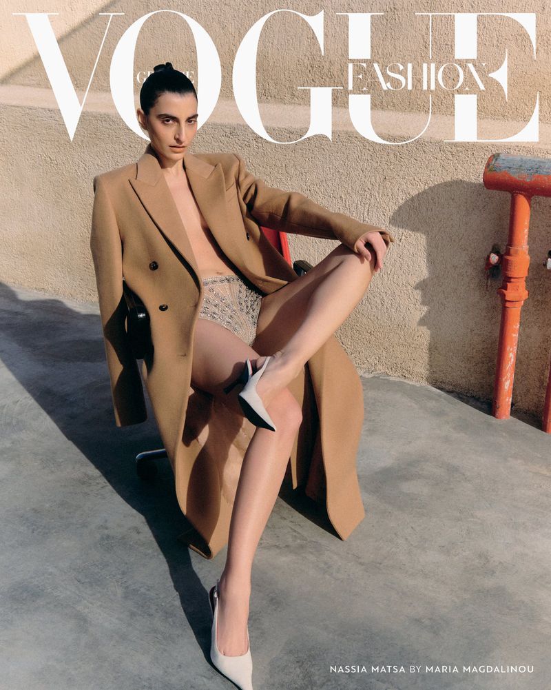 Vogue fashion magazine cover featuring a woman in a coat and briefs, seated on a red chair against a tan wall and concrete floor.