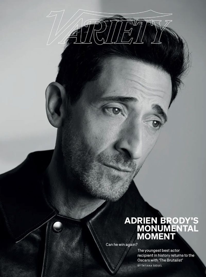 Black and white portrait of Adrien Brody on Variety cover, looking down pensively, wearing a leather jacket against a plain background.