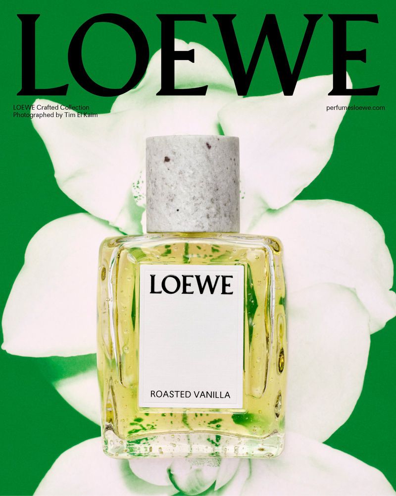 Loewe perfume bottle with Roasted Vanilla scent, displayed with white orchid flowers against a vibrant green backdrop in a studio setting.
