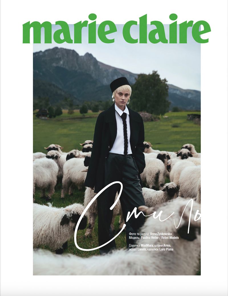 Editorial fashion shot: Woman in dark suit surrounded by sheep in a green mountain pasture for Marie Claire magazine cover.