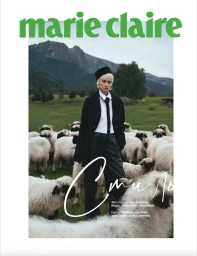 Model with blonde hair wearing a black jacket and white shirt surrounded by sheep in a green meadow for Marie Claire Ukraine