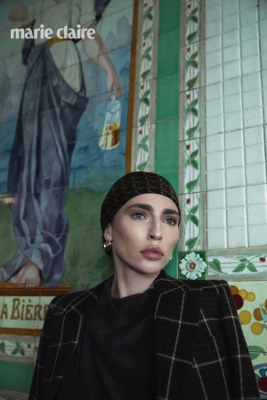 Model in a dark windowpane blazer and patterned headscarf posing in front of a decorative ceramic tile mural.