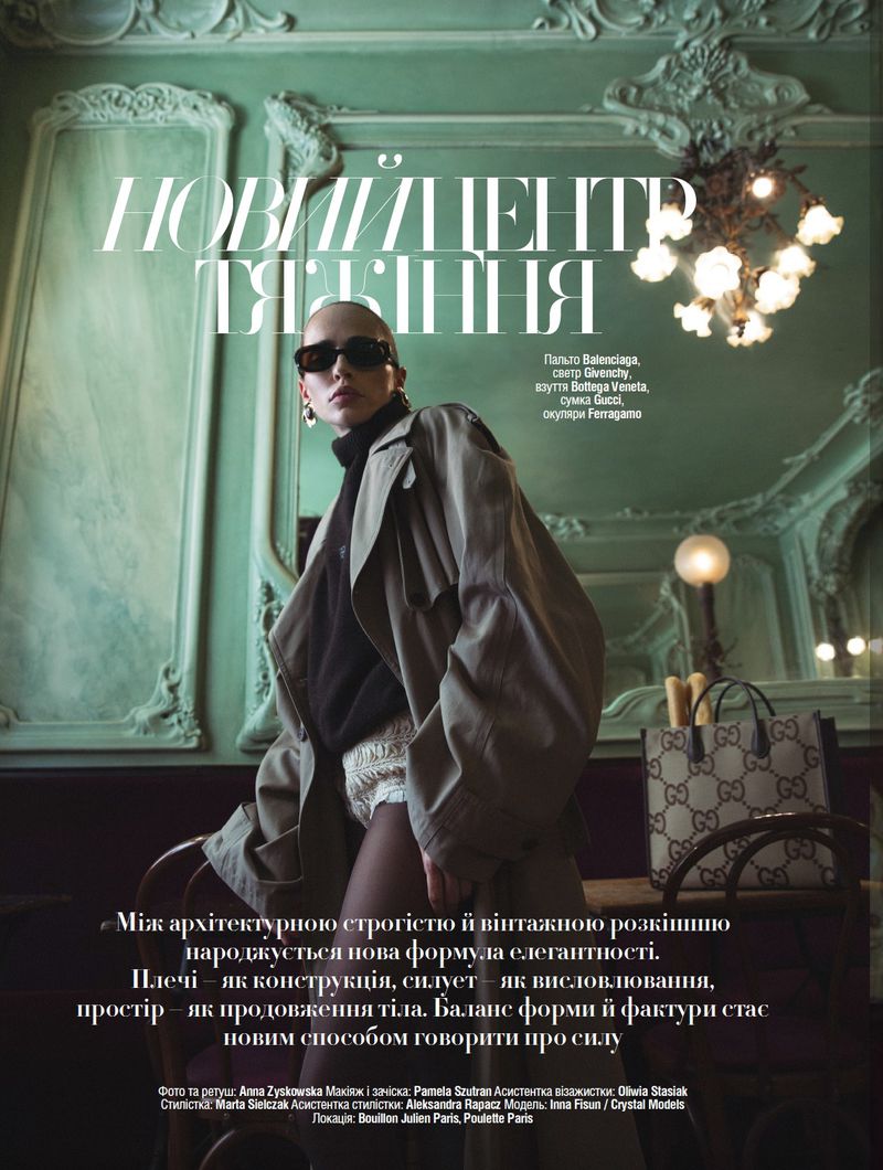 Fashion editorial shot of a young adult female posing in a trench coat with a designer handbag, set against an ornate green background.