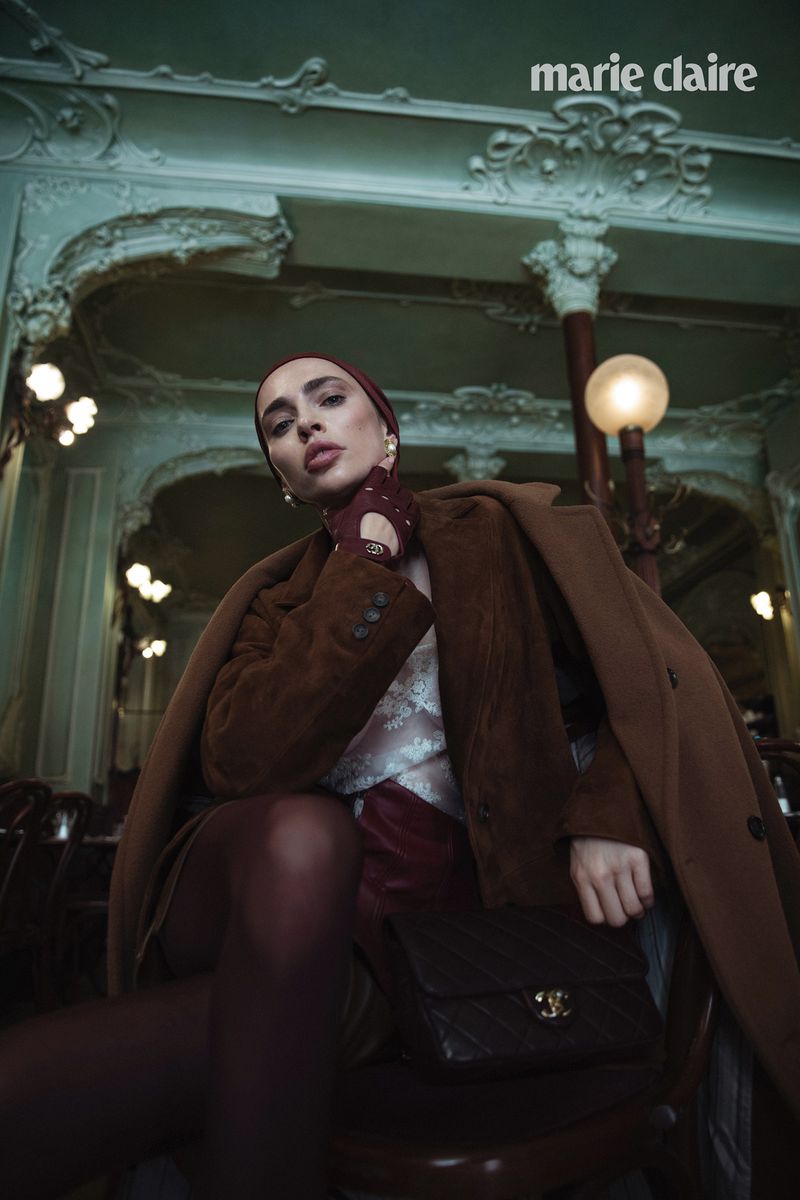 Fashion editorial image in a European cafe featuring a woman wearing a brown coat, headscarf, and Chanel purse in an indoor setting.