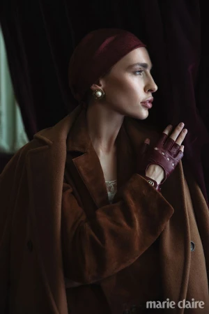 Woman in profile wearing a brown suede coat, burgundy beret, statement pearl earring, and burgundy leather fingerless glove.