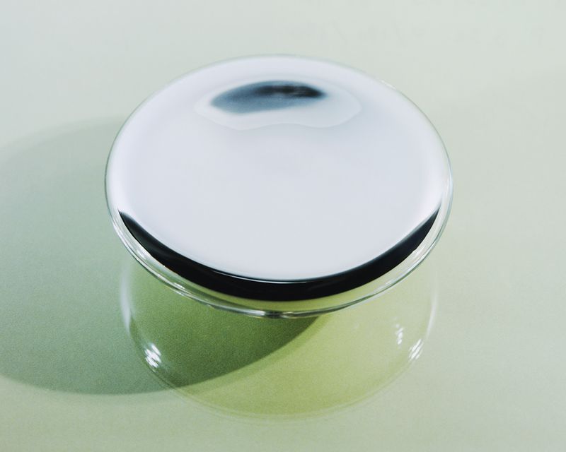 Overhead shot of a shiny, silver container with a round lid, reflecting light and creating a smooth, sleek appearance on a neutral background.