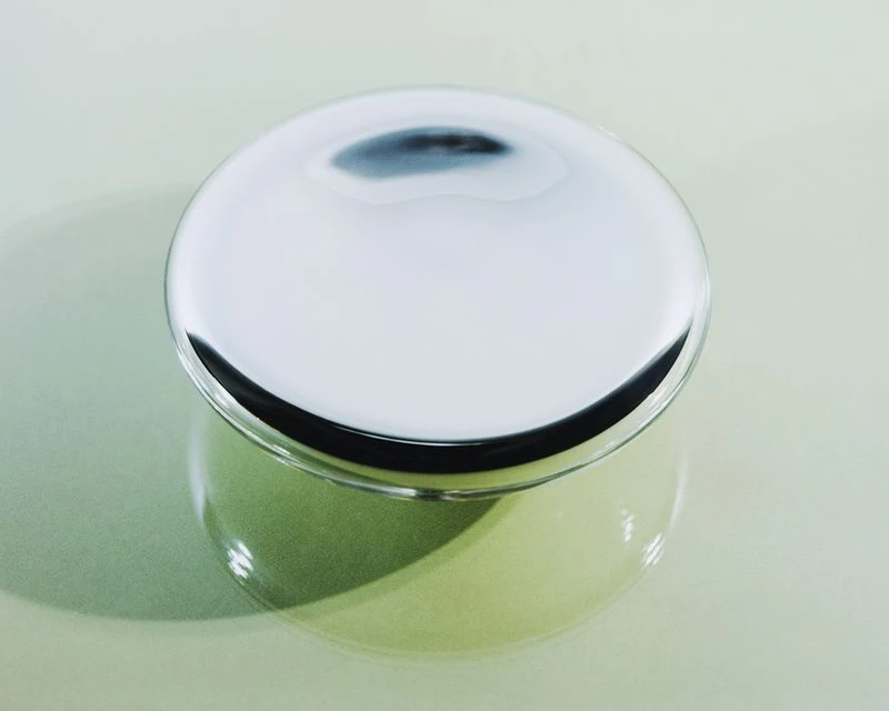 Overhead shot of a shiny, silver container with a round lid, reflecting light and creating a smooth, sleek appearance on a neutral background.