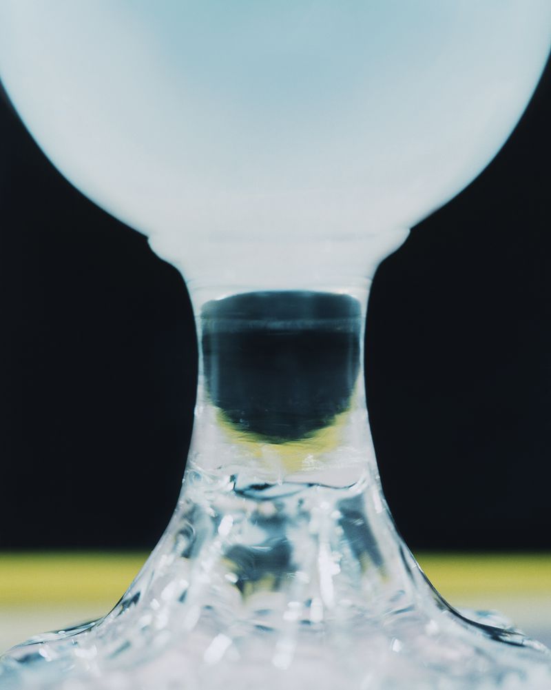 Macro photograph captures the base of a wine glass filled with blue liquid against a black background, creating a striking contrast.