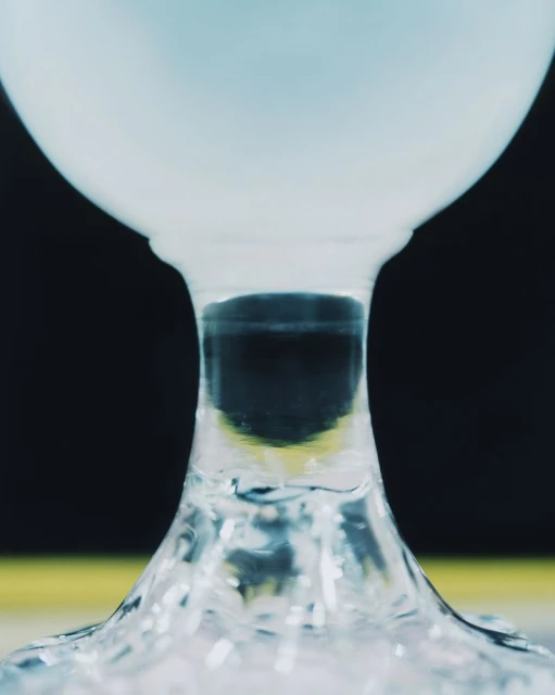 Macro photograph captures the base of a wine glass filled with blue liquid against a black background, creating a striking contrast.