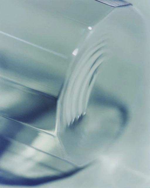 Close-up shot of a clear, geometric glass with a teal hue, emphasizing its textured surface and the play of light and shadow.