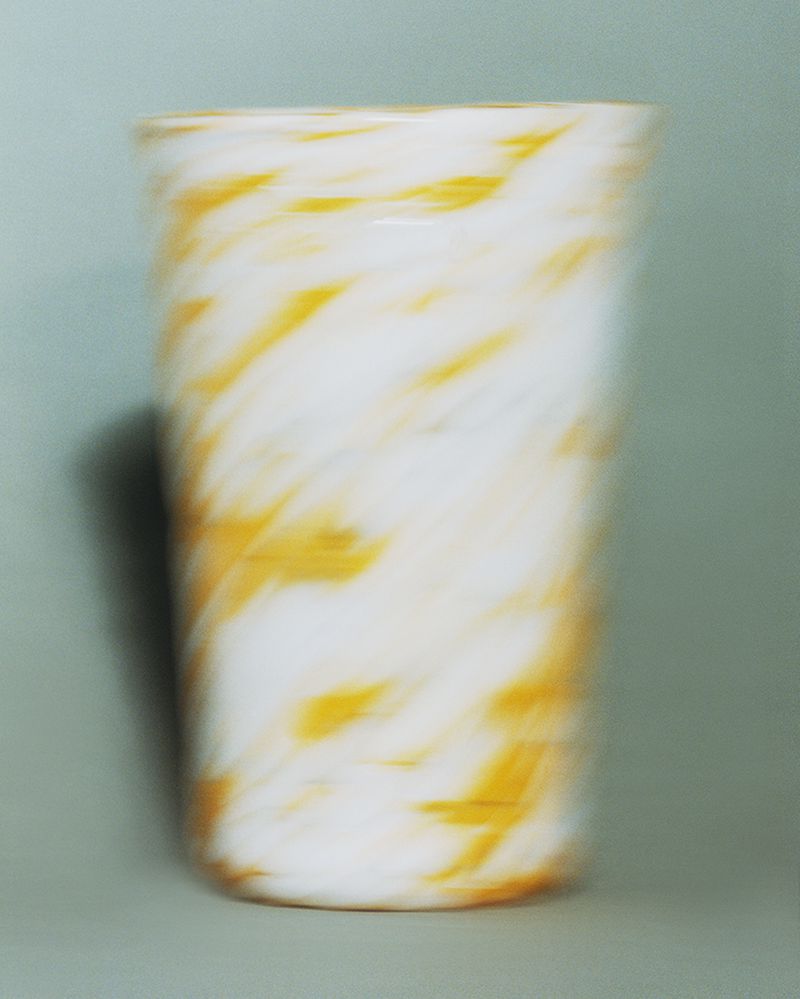 Abstract photography of a white glass with a yellow swirl pattern, captured in a photo studio with a green backdrop.
