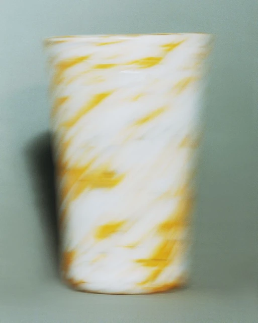 Abstract photography of a white glass with a yellow swirl pattern, captured in a photo studio with a green backdrop.