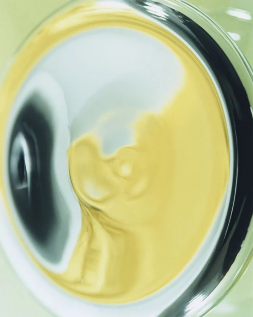 Abstract still life with yellow and blue paint mixing in a glass, capturing swirling patterns and liquid textures with diffused light.