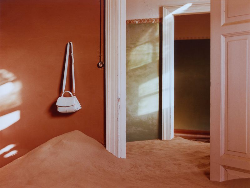 An abandoned room with peach-colored walls and floor, a cream-colored door, and a white purse hanging on the left wall.