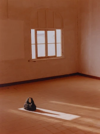 Fashionable black handbag sits in a vacant room with terracotta tile flooring near a window with natural light casting a shadow.