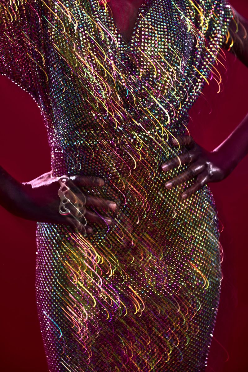 Midsection of a woman posing in a multicolored sequin dress with long exposure light streaks against a red background in a studio.