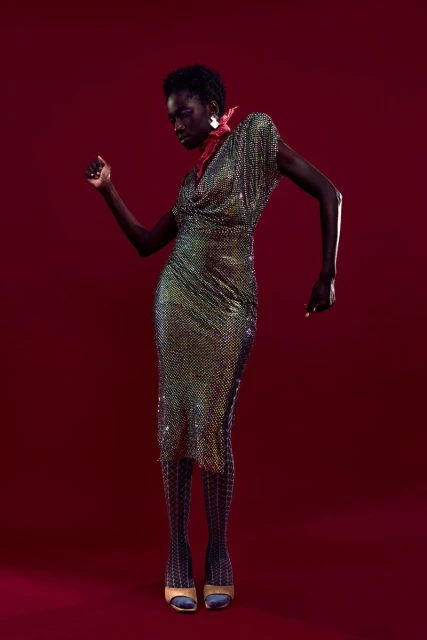 Elegant Black woman in iridescent chainmail dress poses in studio against a maroon background, fashion photography, chic style.